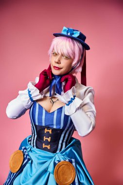 Baştan çıkarıcı, mavi şapkalı ve canlı giyinmiş, pembe arka plandaki kameraya bakan seksi bayan Cosplayer.