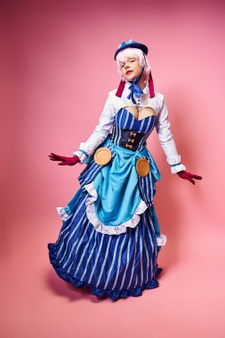 Çekici bayan Cosplayer mavi şapkalı ve canlı giyinmiş pembe arka planda kameraya bakıyor.