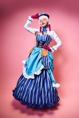 Mavi şapkalı ve canlı giyinmiş, pembe arka plandaki kameraya bakan çekici seksi bayan Cosplayer.