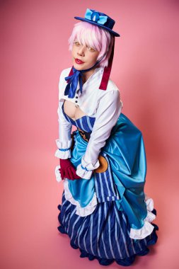 Mavi şapkalı ve canlı giyinmiş, pembe arka plandaki kameraya bakan çekici seksi bayan Cosplayer.