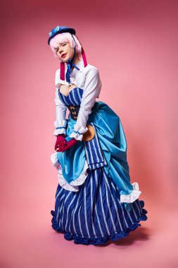 Mavi şapkalı ve canlı giyinmiş, pembe arka planda kameraya bakan çekici seksi bayan kozoyuncu.