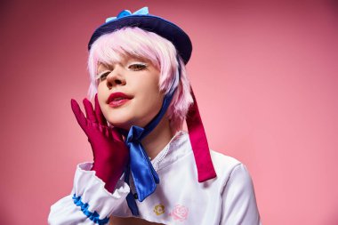 Baştan çıkarıcı seksi bayan Cosplayer mavi şapkalı ve canlı giyinmiş pembe arka planda kameraya bakıyor.