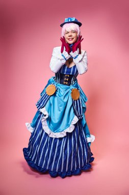 Mavi şapkalı şık bayan Cosplayer ve pembe arka planda kameraya bakan canlı elbise.
