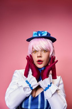 Mavi şapkalı ve canlı elbiseli çekici, şık bayan Cosplayer pembe arka planda kameraya bakıyor.