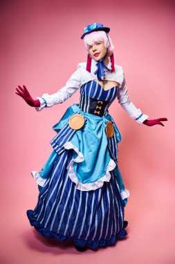 Mavi şapkalı, parlak elbiseli, pembe arka planda kameraya bakan çekici bir bayan Cosplayer.
