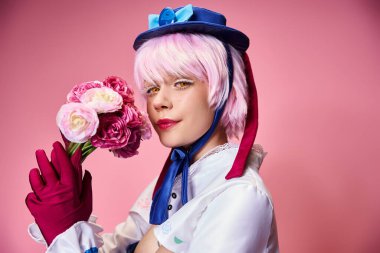 Çekici, canlı kostümlü, elinde pembe çiçeklerle kameraya bakan güzel bir bayan oyuncu.