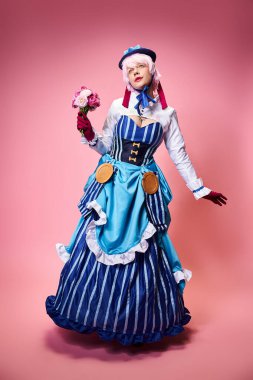 Çekici, canlı giyinmiş, elinde pembe çiçekler olan ve pembe arka plana bakan kadın Cosplayer.