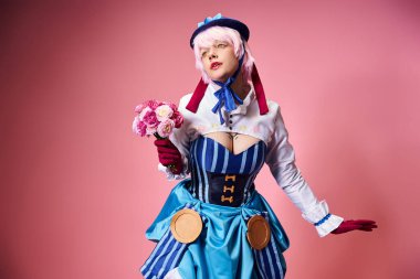 Çekici, canlı giyinmiş, elinde pembe çiçekler olan ve pembe arka plana bakan kadın Cosplayer.