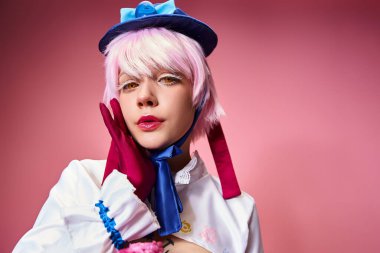 Güzel görünümlü, şık, mavi şapkalı, parlak elbiseli, pembe arka planda kameraya bakan kadın bir Cosplayer.