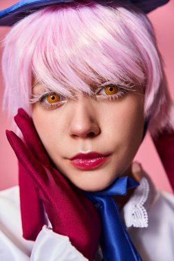 Güzel görünümlü, şık, mavi şapkalı, parlak elbiseli, pembe arka planda kameraya bakan kadın bir Cosplayer.