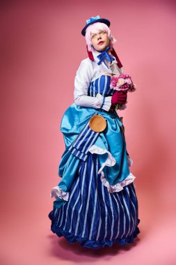 Canlı giyinmiş, elinde pembe çiçeklerle pembe arka plana bakan şık bayan Cosplayer.