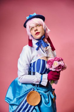 Canlı giyinmiş, elinde pembe çiçeklerle pembe arka plana bakan şık bayan Cosplayer.