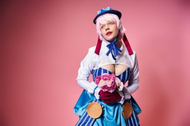 Canlı giyinmiş, elinde pembe çiçeklerle pembe arka plana bakan sevimli, modaya uygun bayan Cosplayer.