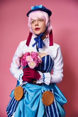 Canlı giyinmiş, elinde pembe çiçeklerle pembe arka plana bakan şık, şık bir bayan Cosplayer.