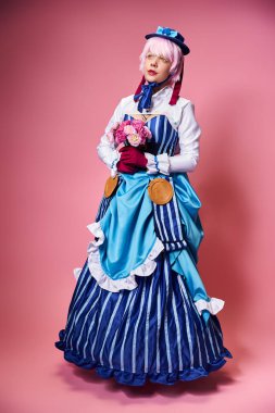 cute stylish female cosplayer in vivid attire holding pink flowers and looking away on pink backdrop clipart