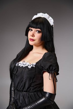 luscious sexy female cosplayer in tempting maid costume looking at camera on gray background clipart