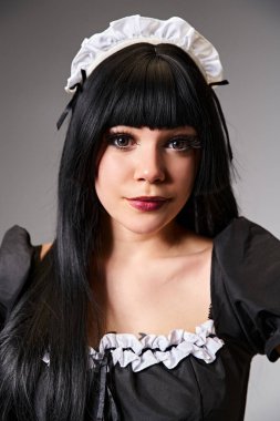 Çekici hizmetçi kostümü içinde büyüleyici kadın Cosplayer gri arka plandaki kameraya bakıyor.