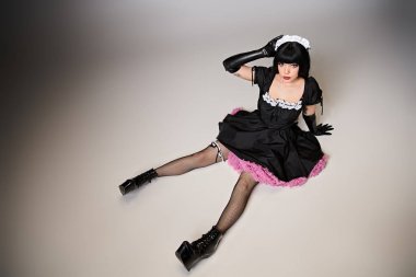 Cazip hizmetçi kostümlü çekici seksi kadın Cosplayer gri arka plandaki kameraya bakıyor.