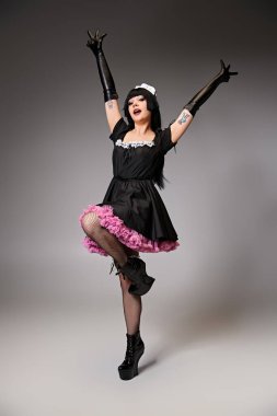 Güzel görünümlü seksi bayan Cosplayer çekici hizmetçi kostümü içinde gri arka plandaki kameraya bakıyor.