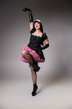 Çekici seksi bayan Cosplayer çekici hizmetçi kostümü içinde gri arka plandaki kameraya bakıyor.