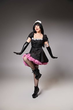 Güzel, genç bir kadın kostümlü, alımlı bir şekilde poz veren ve gri arka plana bakan genç bir Cosplayer.