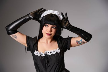 Neko kulakları gösteren hizmetçi kostümlü ve gri arka plana bakan baştan çıkarıcı bir kadın.