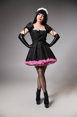 Çekici, genç bir kadın kostümlü, alımlı poz veren ve gri arka plana bakan.