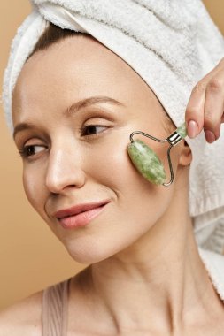 A woman with a towel on her head indulges in self-care with a face roller, radiating tranquility and natural beauty. clipart