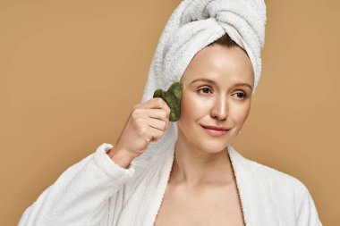 Başında havlu olan çarpıcı bir kadın gua sha tutuyor..