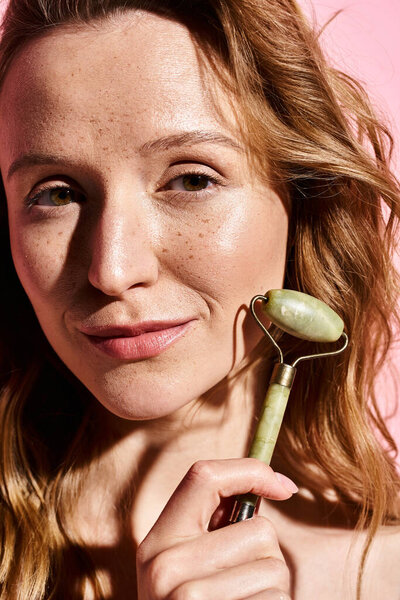 A natural beauty woman poses while holding face roller and looking directly at the camera, showcasing her elegance.