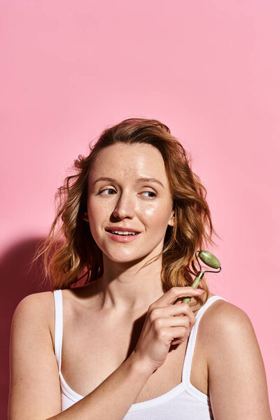 An attractive woman in a white tank top gracefully holding a delicate face roller.