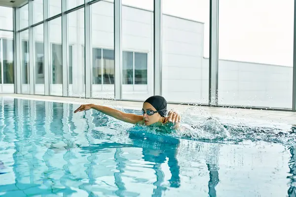一位身穿泳衣 头戴泳帽的年轻女子优雅地在大楼内的一个室内游泳池里游泳 — 图库照片