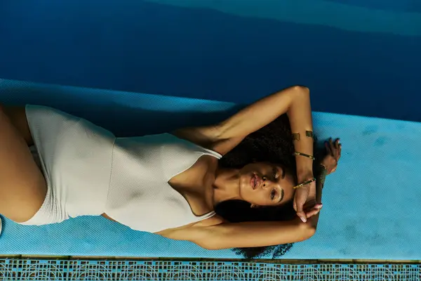 stock image Top view of pretty african american woman in bathing suit lying by the pool, exuding tranquility