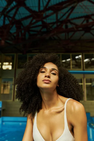 stock image alluring young and curly african american woman in bathing suit standing and looking at camera