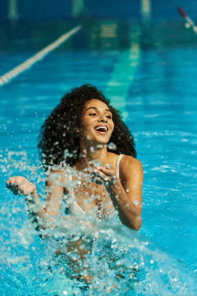 Koyu tenli kadın havuzun içine su sıçratıyor, tatilde keyif ve mutluluktan zevk alıyor.