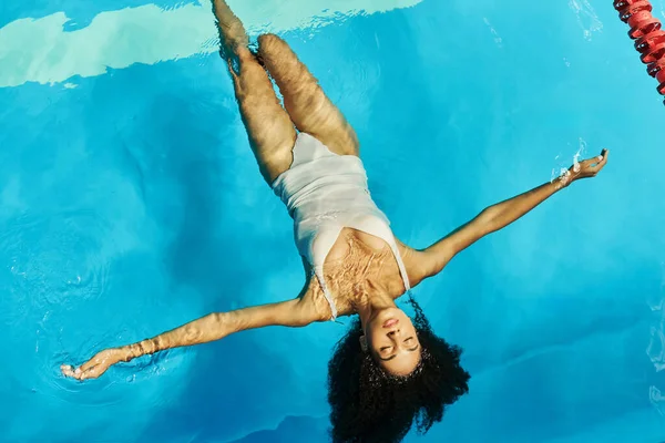 stock image top view of peaceful african american woman swimming on her back in clear pool water, tranquility