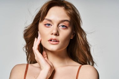Doğal makyajlı güzel bir kadın, yüzüne dokunan kameraya bakıyor.