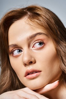 Şeftali rengi doğal makyajlı güzel bir kadının yakın plan portresi gri arka planda çeneye dokunuyor.