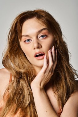 Şeftali tüyü. Mavi gözlü çekici bir kadın, gri arka planda yanağına dokunuyor.