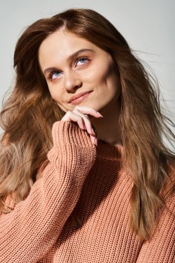 Neşeli gülümseyen kadın çıplak şeftali makyajıyla başını kaldırıyor, gri arka planda çenesine dokunuyor.