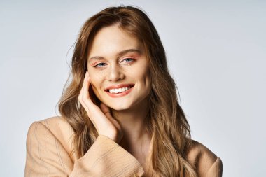 Gri arka planda gözyaşı şekilli yüz mücevherleri olan bej ceketli çekici kadın, şeftali tüyü.