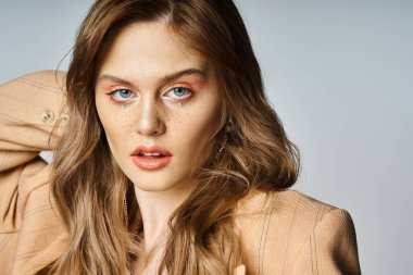 Bej ceketli, yırtık pırtık yüzlü, kameraya bakan güzel bir kadın portresi.