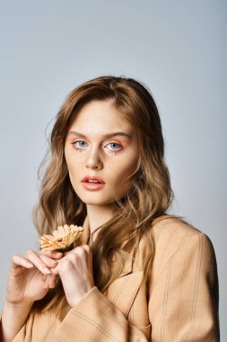 Çekici kadın portresi kameraya bakıyor ve papatya tutuyor şeftali makyajı yapıyor, yüz mücevherleri takıyor.