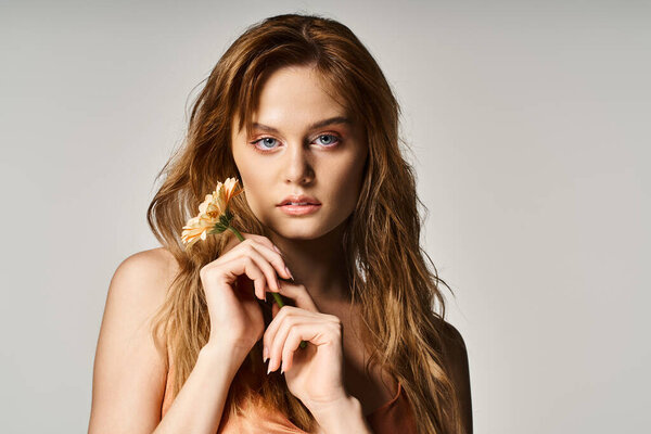 Beauty portrait of sexy woman with blue eyes, with gerbera daisy near face on grey background