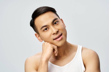 Gri bir stüdyoda, kolsuz bluz giyerken poz veren yakışıklı bir Asyalı..