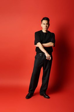 A stylish and handsome Asian man stands confidently in front of a bold red background in a studio setting. clipart