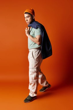 Şık giyinmiş yakışıklı bir Asyalı sırt çantasını stüdyo ortamında turuncu bir arka plana taşıyor..