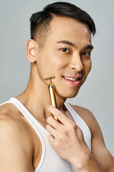 一个亚洲男人在灰色工作室里拿着一把金色剃须刀 展示着财富和优雅 — 图库照片
