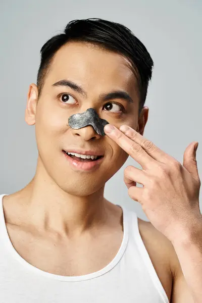 彼のスキンケアのルーチンのための美しさの鼻パッチを持つ灰色のスタジオでハンサムなアジア人男性 — ストック写真