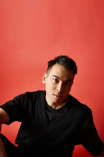 stock image A stylish and handsome Asian man in a black shirt stands confidently against a vibrant red wall in a studio.
